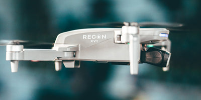 Sort Drone Recon XV1 i luften over en græsmark med tændte LED-lys.