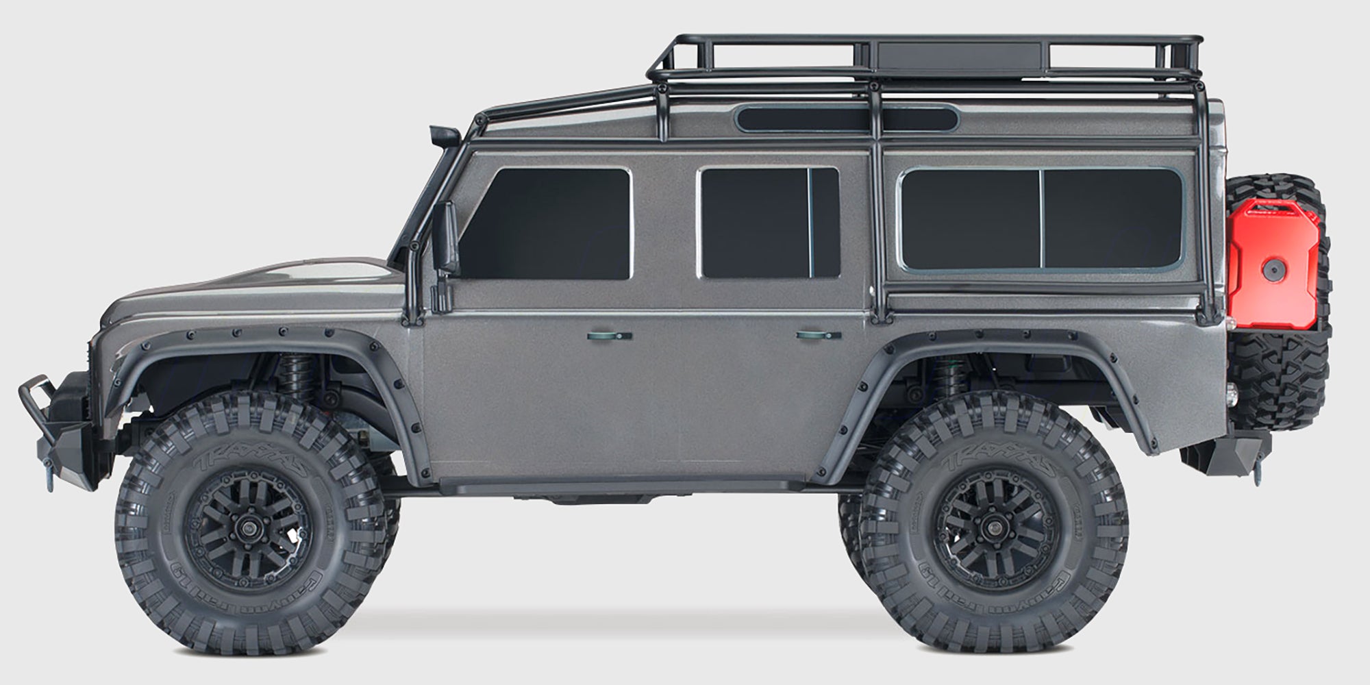 Grå Traxxas TRX-4 Land Rover Defender crawler kører gennem mudret terræn i naturen.